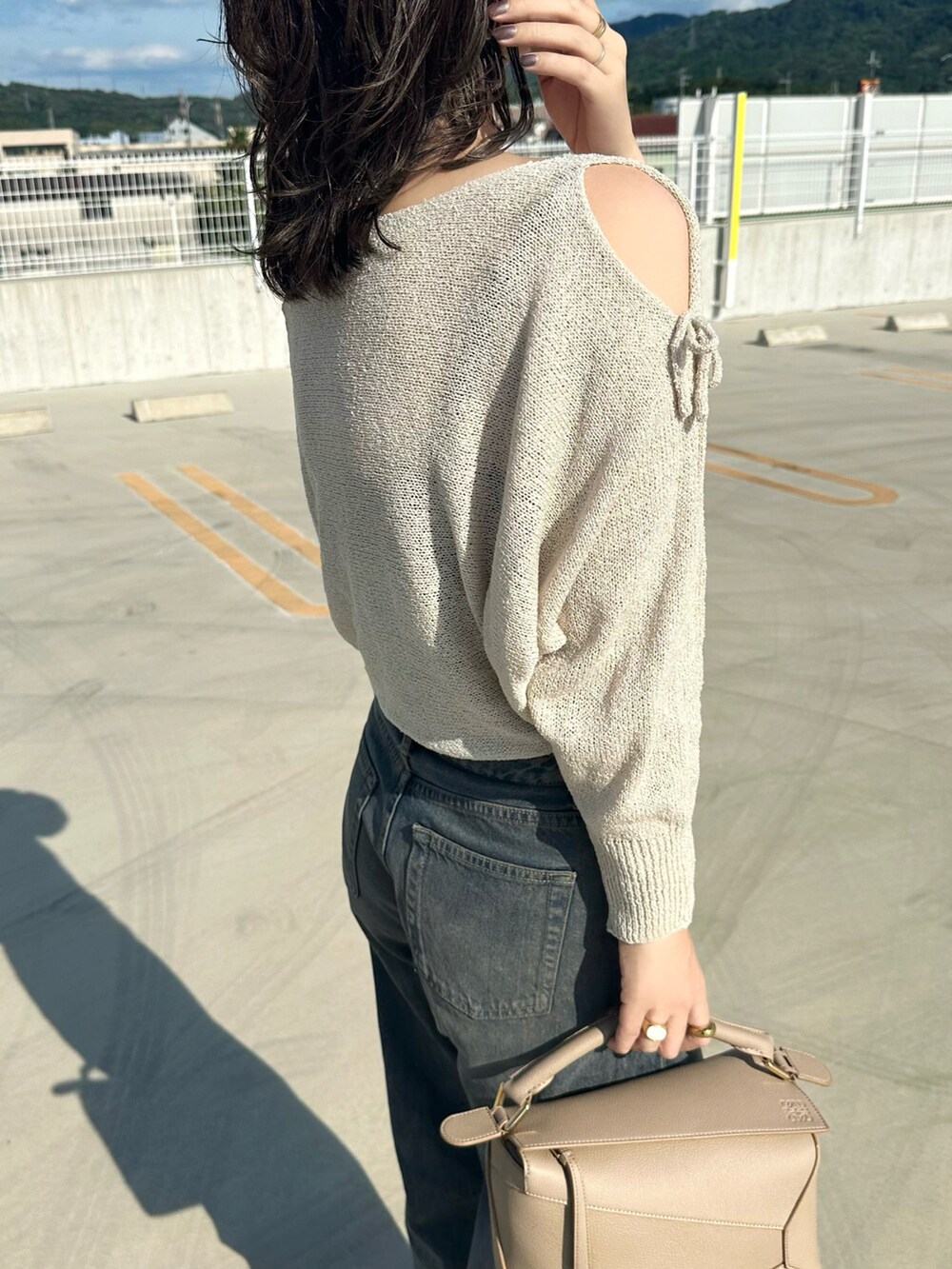 ベージュ系のニット/セーター、ブルー系のデニムパンツ、ベージュ系のショルダーバッグを着用したレディースの夏コーディネートの5枚目の写真