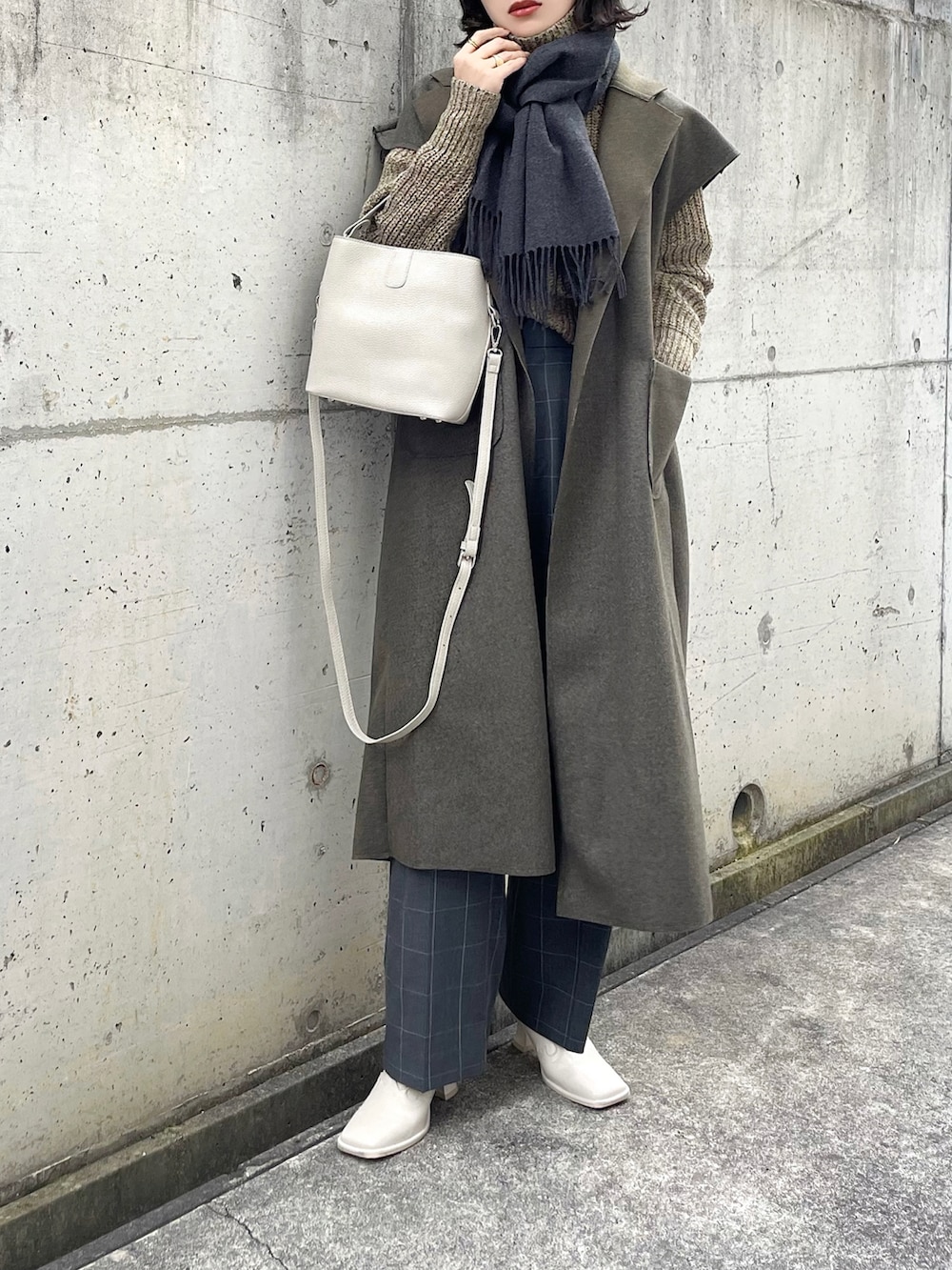 ベージュ系のハンドバッグ、ブラウン系のベスト、グレー系のパンツを着用したレディースの冬コーディネートの2枚目の写真