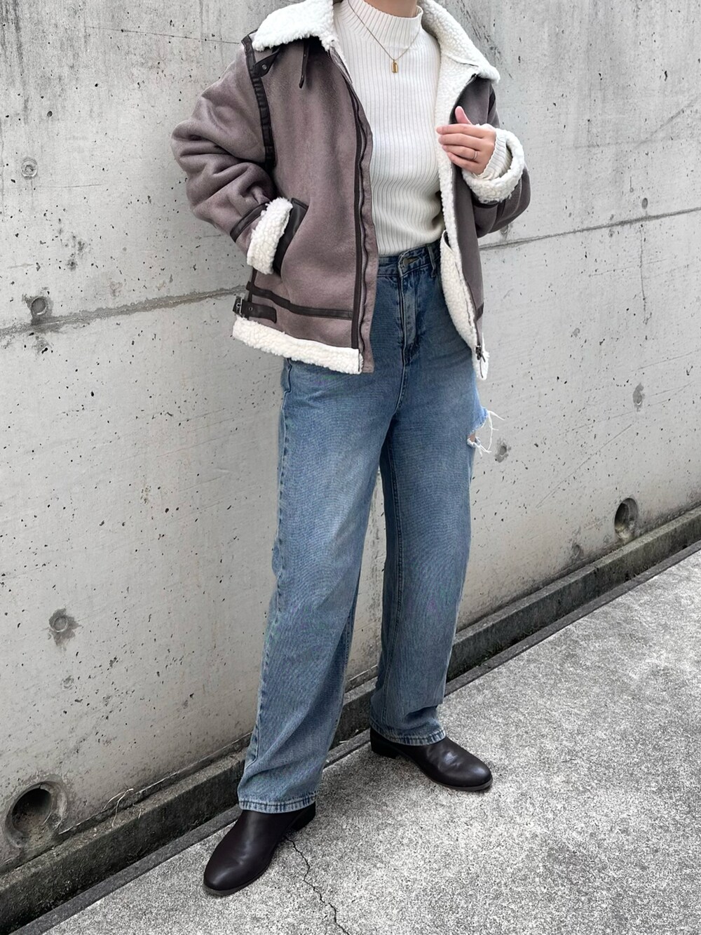 グレー系のムートンコート、ホワイト系のニット/セーター、ブルー系のデニムパンツを着用したレディースの冬コーディネートの2枚目の写真