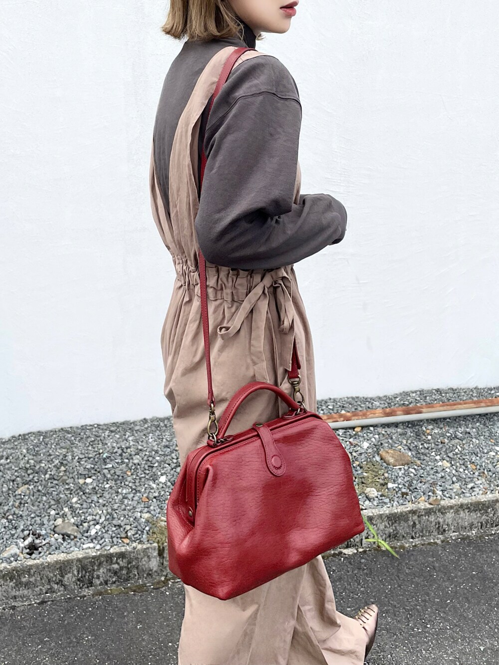 レッド系のショルダーバッグ、ベージュ系のオールインワン・サロペット、グレー系のパンプスを着用したレディースの秋コーディネートの2枚目の写真