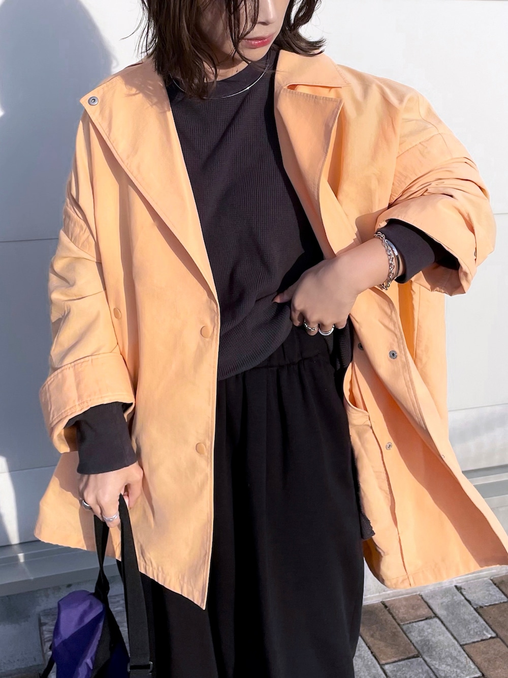 オレンジ系のポンチョ、グレー系のTシャツ/カットソー、ブラック系のパンツを着用したレディースの春コーディネートの3枚目の写真