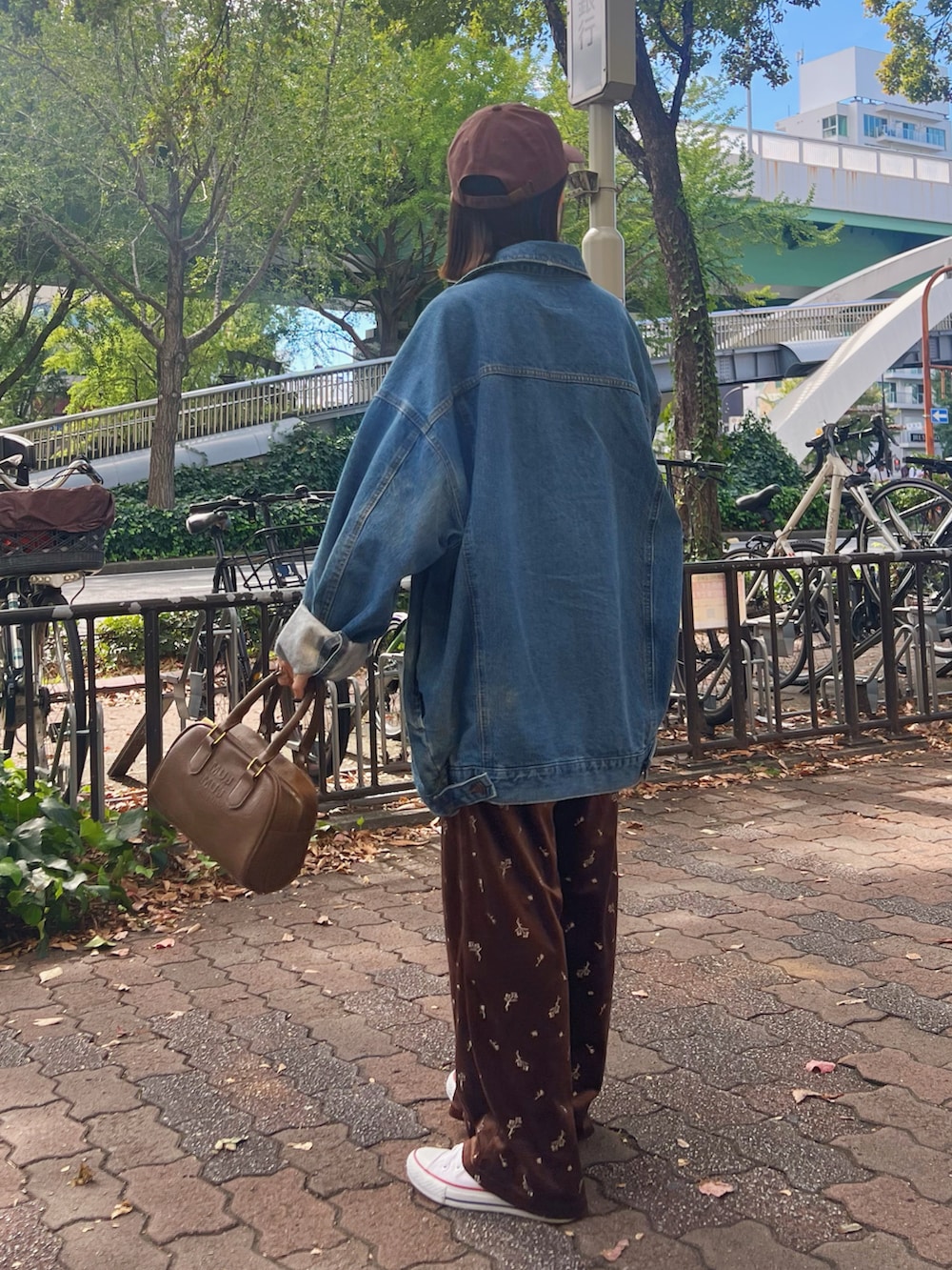 ホワイト系のスニーカー、ブルー系のデニムジャケット、ブラウン系のボストンバッグを着用したレディースの秋コーディネートの2枚目の写真