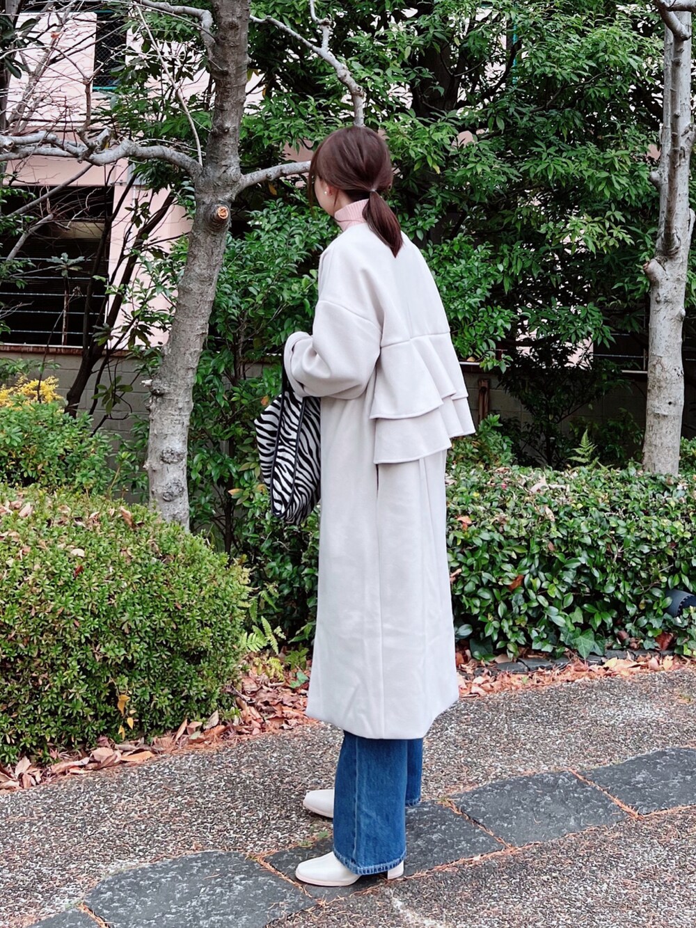 グレー系のノーカラーコート、ピンク系のニット/セーター、ブルー系のデニムパンツを着用したレディースの冬コーディネートの2枚目の写真