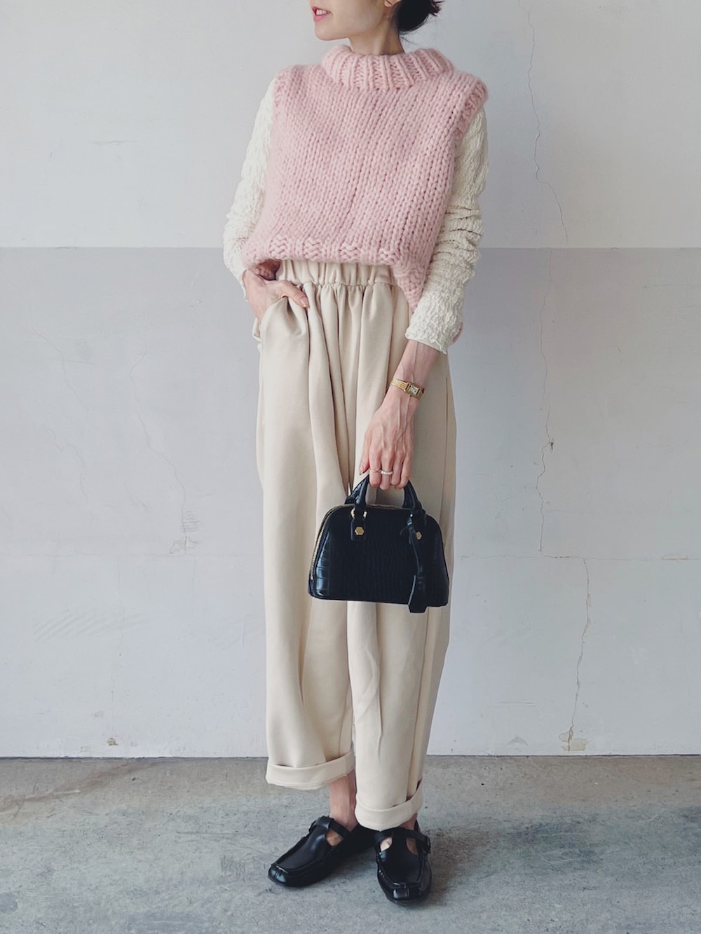 ピンク系のベスト、ブラック系のショルダーバッグ、ベージュ系のパンツを着用したレディースの春コーディネートの2枚目の写真