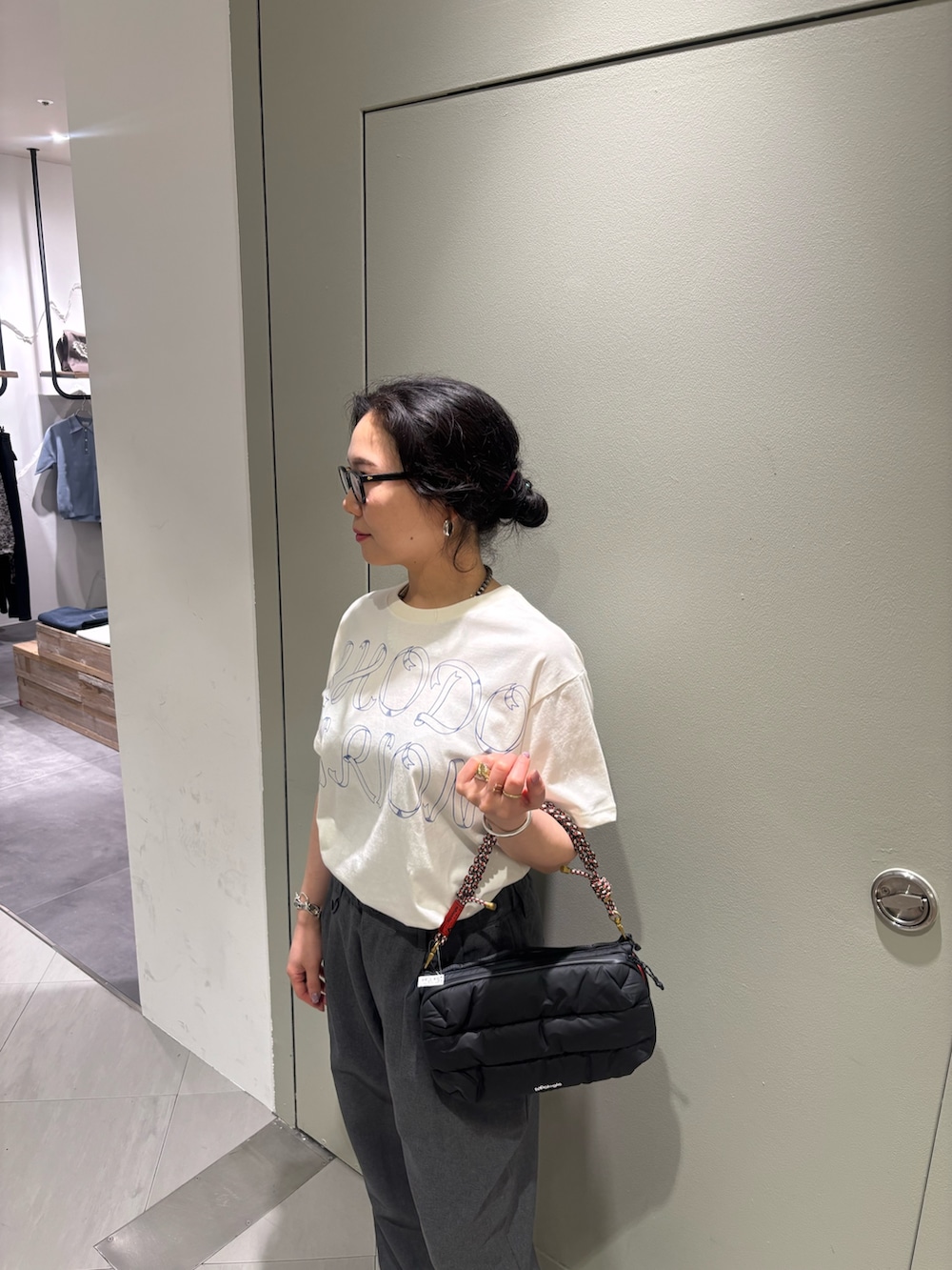 グレー系のスラックス、ブラック系のショルダーバッグ、ブラック系のモカシン/デッキシューズを着用したレディースの夏コーディネートの2枚目の写真