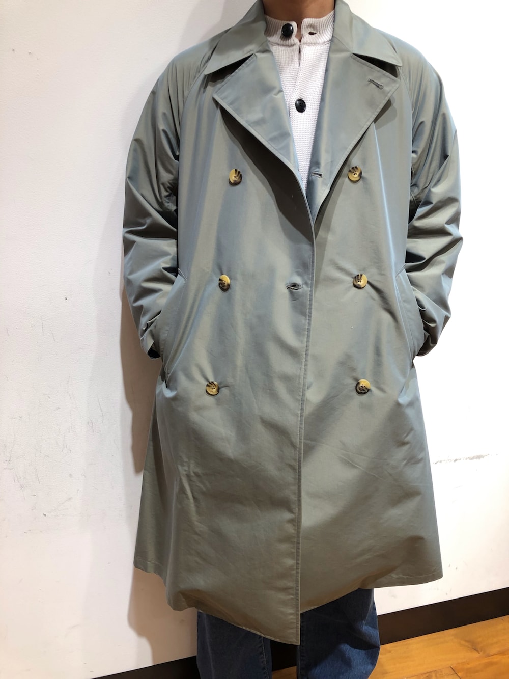 グレー系のニット/セーター、グリーン系のステンカラーコート、ブルー系のシューズを着用したメンズの冬コーディネートの2枚目の写真