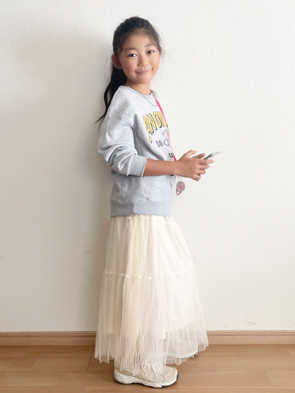 ホワイト系のスカート、ピンク系のスマホグッズを着用したキッズの秋コーディネートの2枚目の写真