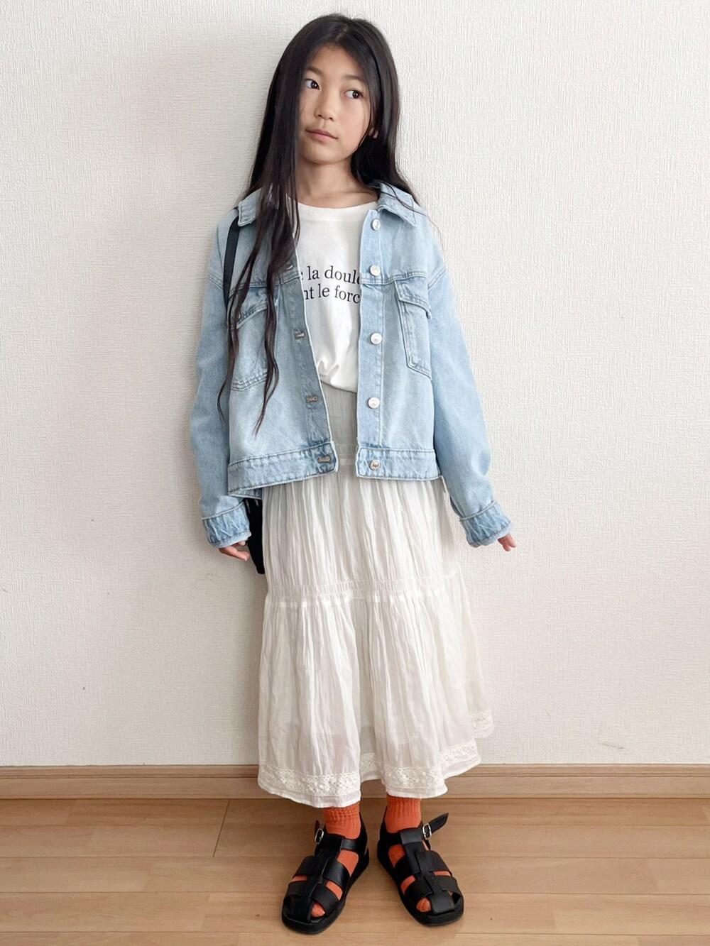 ブルー系のデニムジャケット、ホワイト系のスカート、ブラック系のサンダルを着用したキッズの春コーディネートの3枚目の写真
