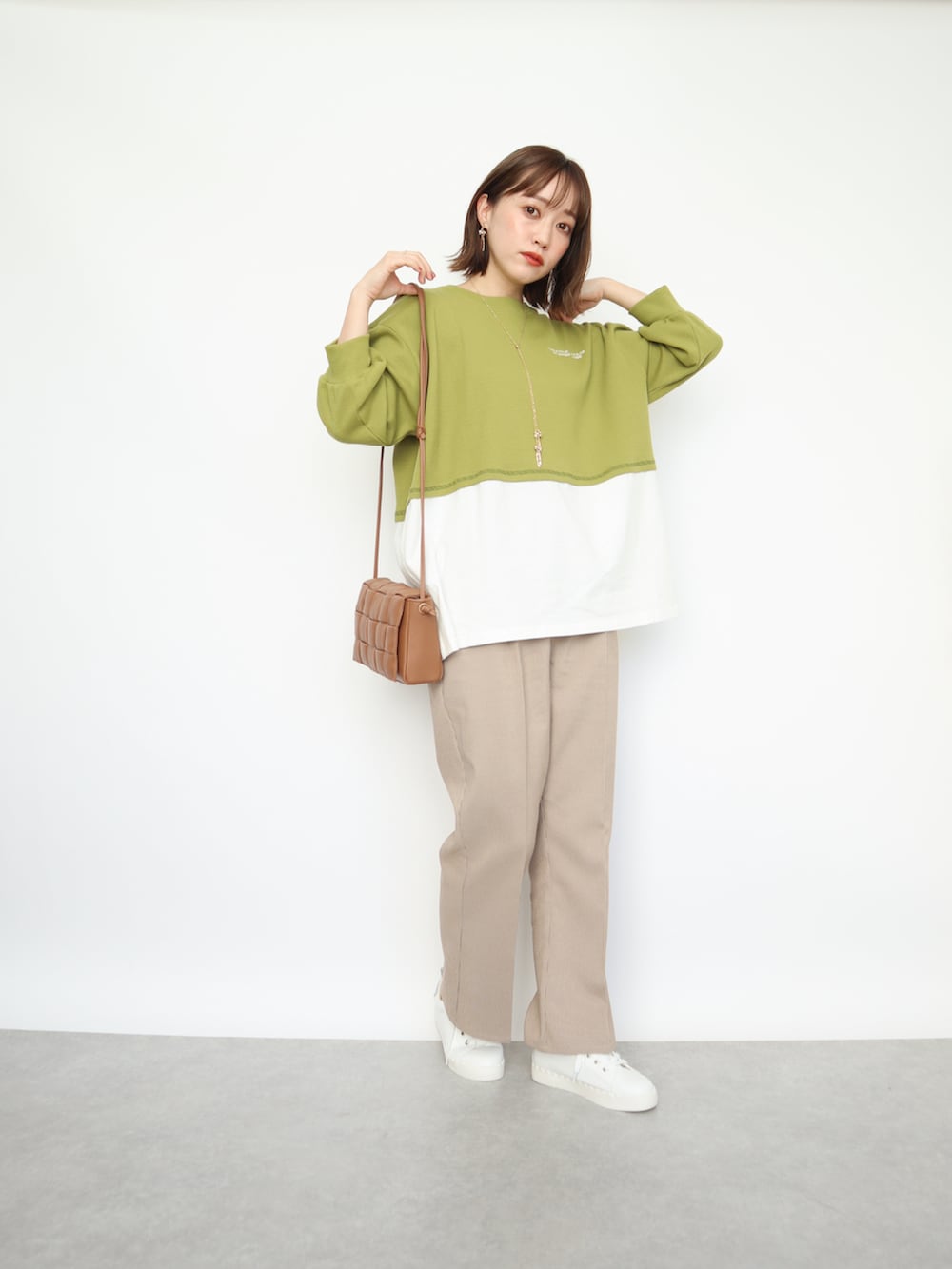 グリーン系のトップス、ベージュ系のパンツ、ブラウン系のバッグを着用したレディースの春コーディネートの2枚目の写真