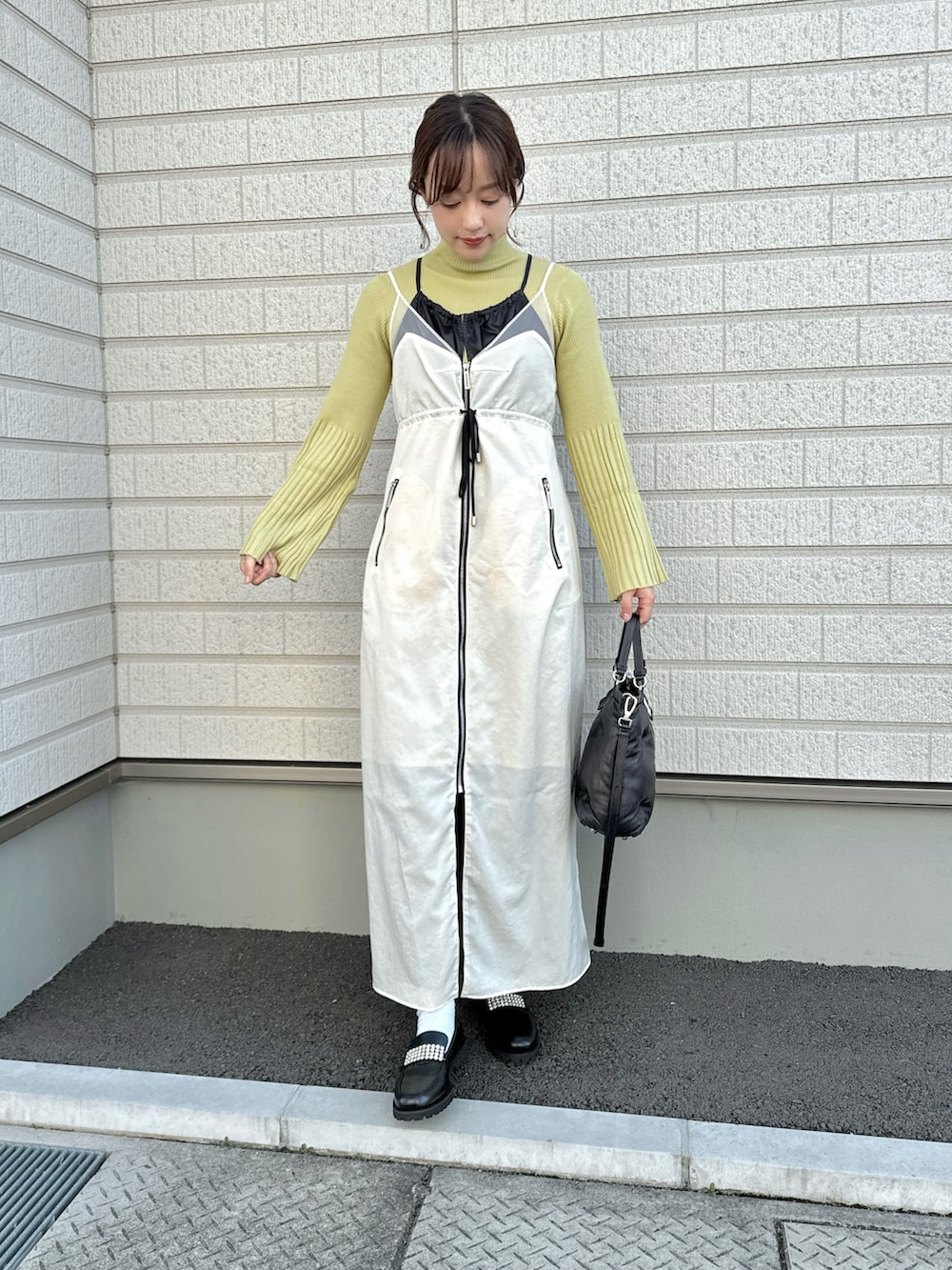 グリーン系のニット/セーター、ブラック系のジャケット/アウター、ホワイト系のジャンパースカートを着用したレディースの秋コーディネートの2枚目の写真