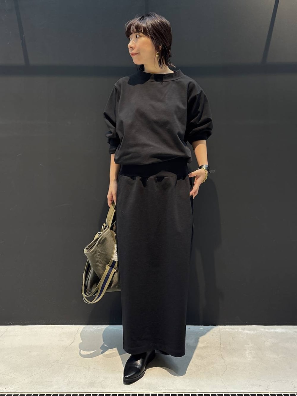 グリーン系のトートバッグ、ブラック系のワンピース、ブラック系のブレスレットを着用したレディースの冬コーディネートの6枚目の写真