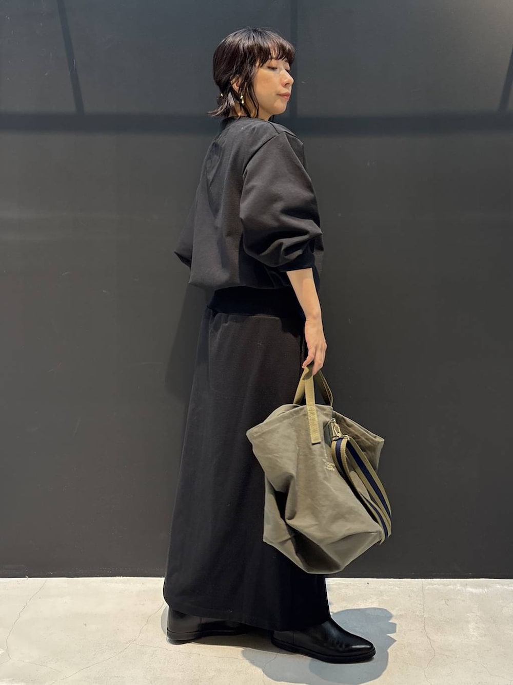 グリーン系のトートバッグ、ブラック系のワンピース、ブラック系のブレスレットを着用したレディースの冬コーディネートの4枚目の写真