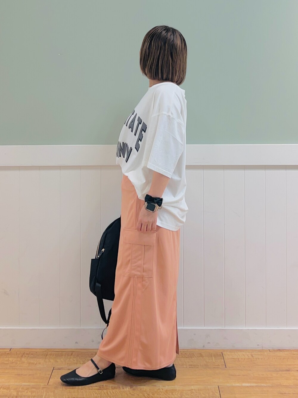 ブラック系のバックパック/リュック、ホワイト系のTシャツ/カットソー、オレンジ系のスカートを着用したレディースの夏コーディネートの2枚目の写真