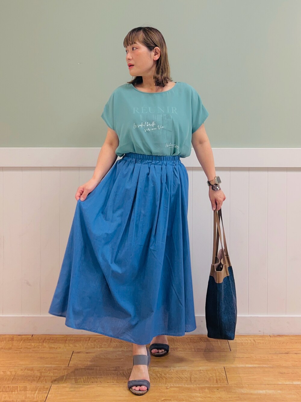 グリーン系のTシャツ/カットソー、ブラウン系のトートバッグ、ブルー系のスカートを着用したレディースの夏コーディネートの3枚目の写真