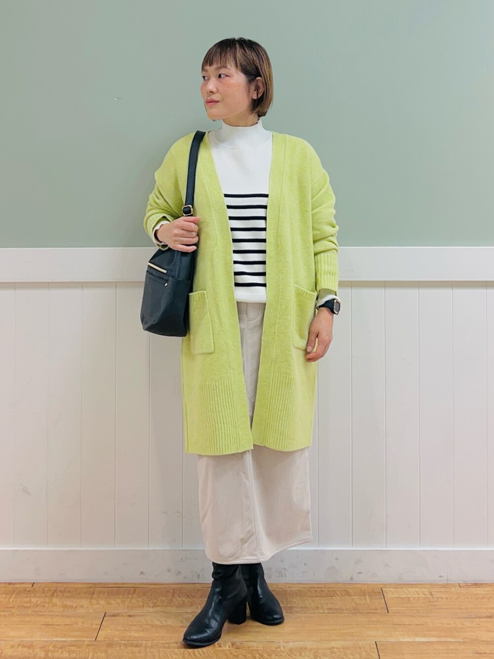 ブラック系のニット/セーター、イエロー系のカーディガン/ボレロ、ベージュ系のスカートを着用したレディースの秋コーディネートの2枚目の写真