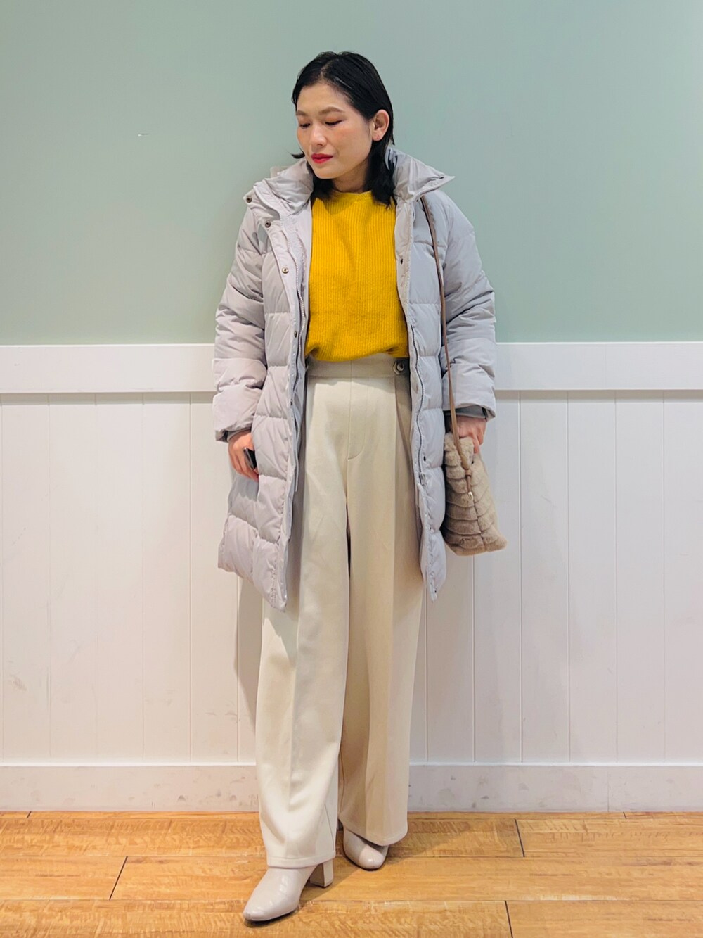 イエロー系のニット/セーター、ベージュ系のダウンジャケット/コート、ベージュ系のショルダーバッグを着用したレディースの冬コーディネートの4枚目の写真