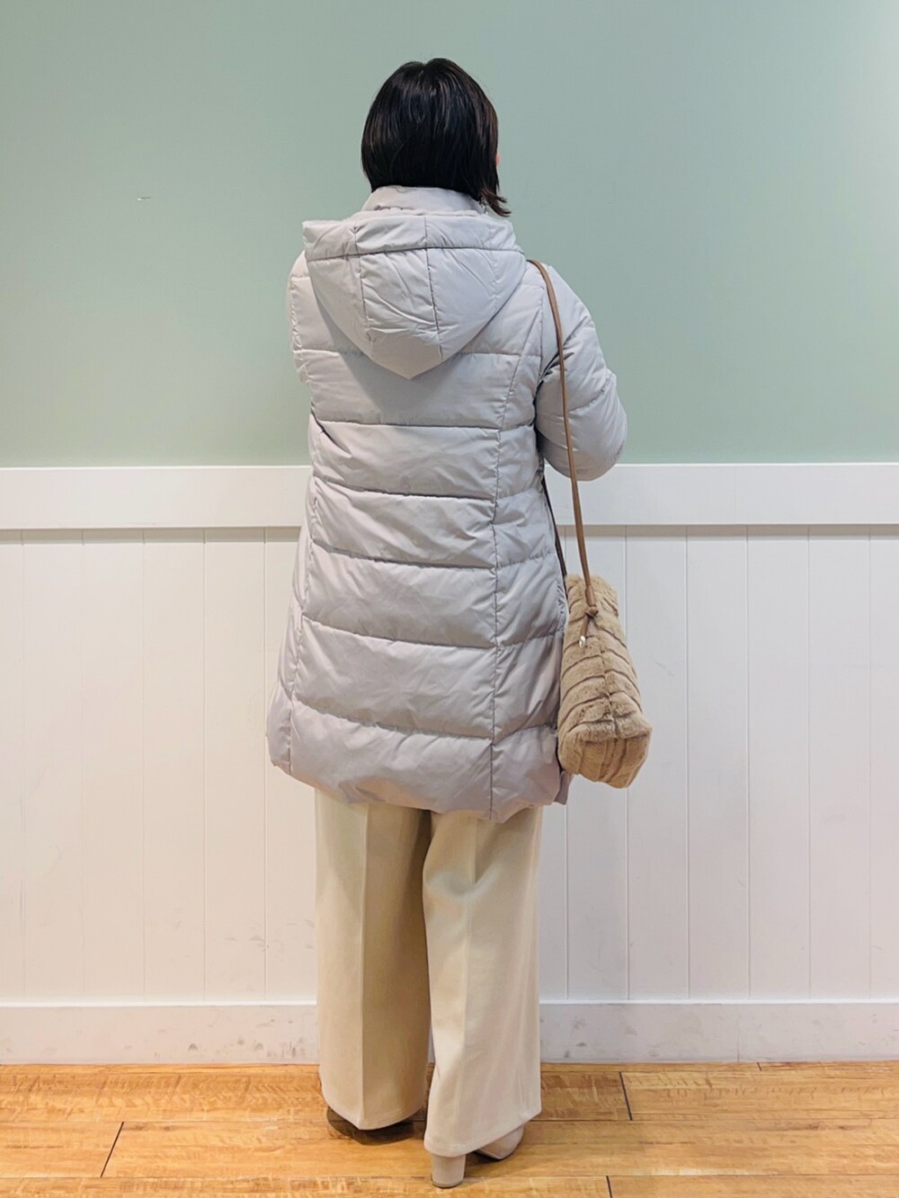 イエロー系のニット/セーター、ベージュ系のダウンジャケット/コート、ベージュ系のショルダーバッグを着用したレディースの冬コーディネートの2枚目の写真