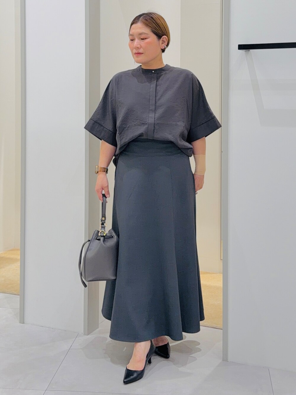 ブラック系のシャツ/ブラウス、グレー系のスカート、グレー系のショルダーバッグを着用したレディースの夏コーディネートの2枚目の写真