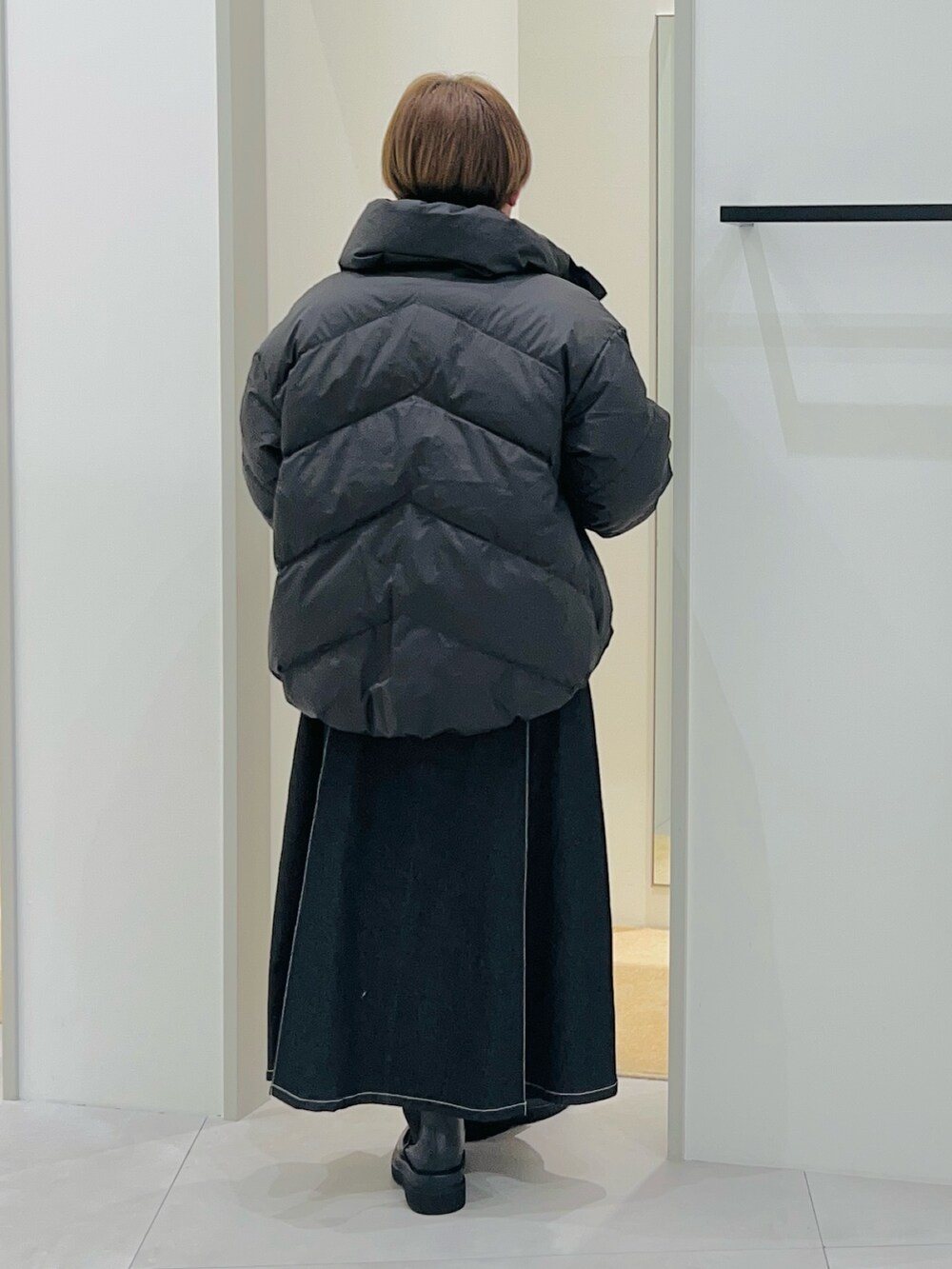 ブラック系のダウンジャケット/コート、オレンジ系のニット/セーター、ブラック系のデニムスカートを着用したレディースの秋コーディネートの4枚目の写真