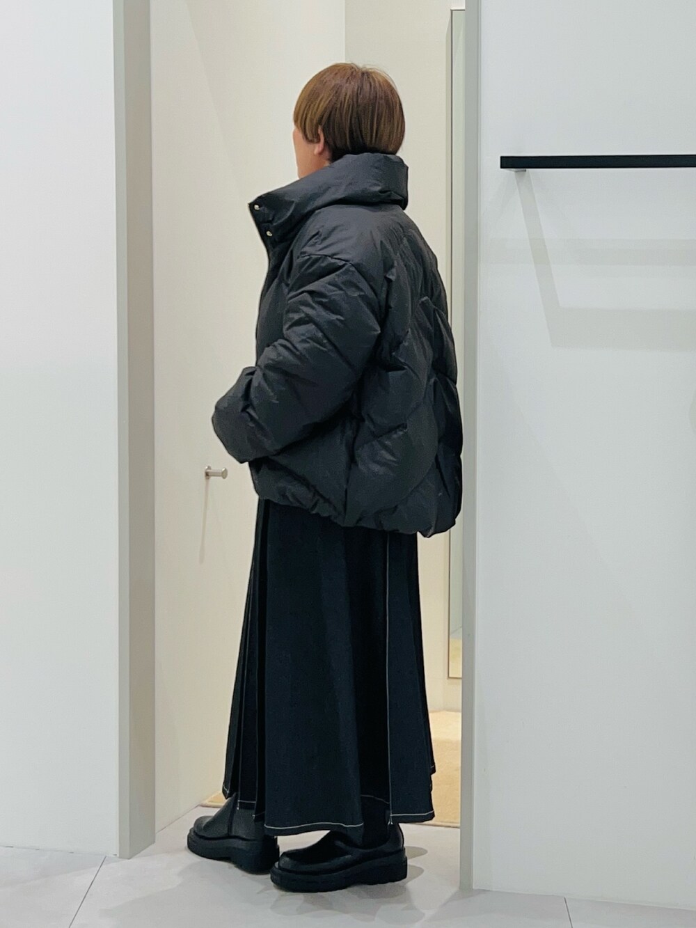 ブラック系のダウンジャケット/コート、オレンジ系のニット/セーター、ブラック系のデニムスカートを着用したレディースの秋コーディネートの3枚目の写真