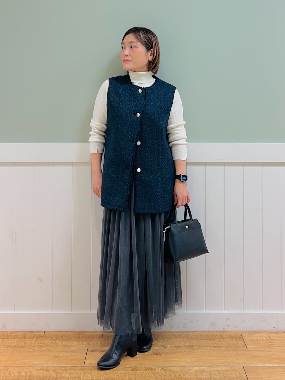 ホワイト系のニット/セーター、ブルー系のベスト、ブラック系のトートバッグを着用したレディースの冬コーディネートの2枚目の写真