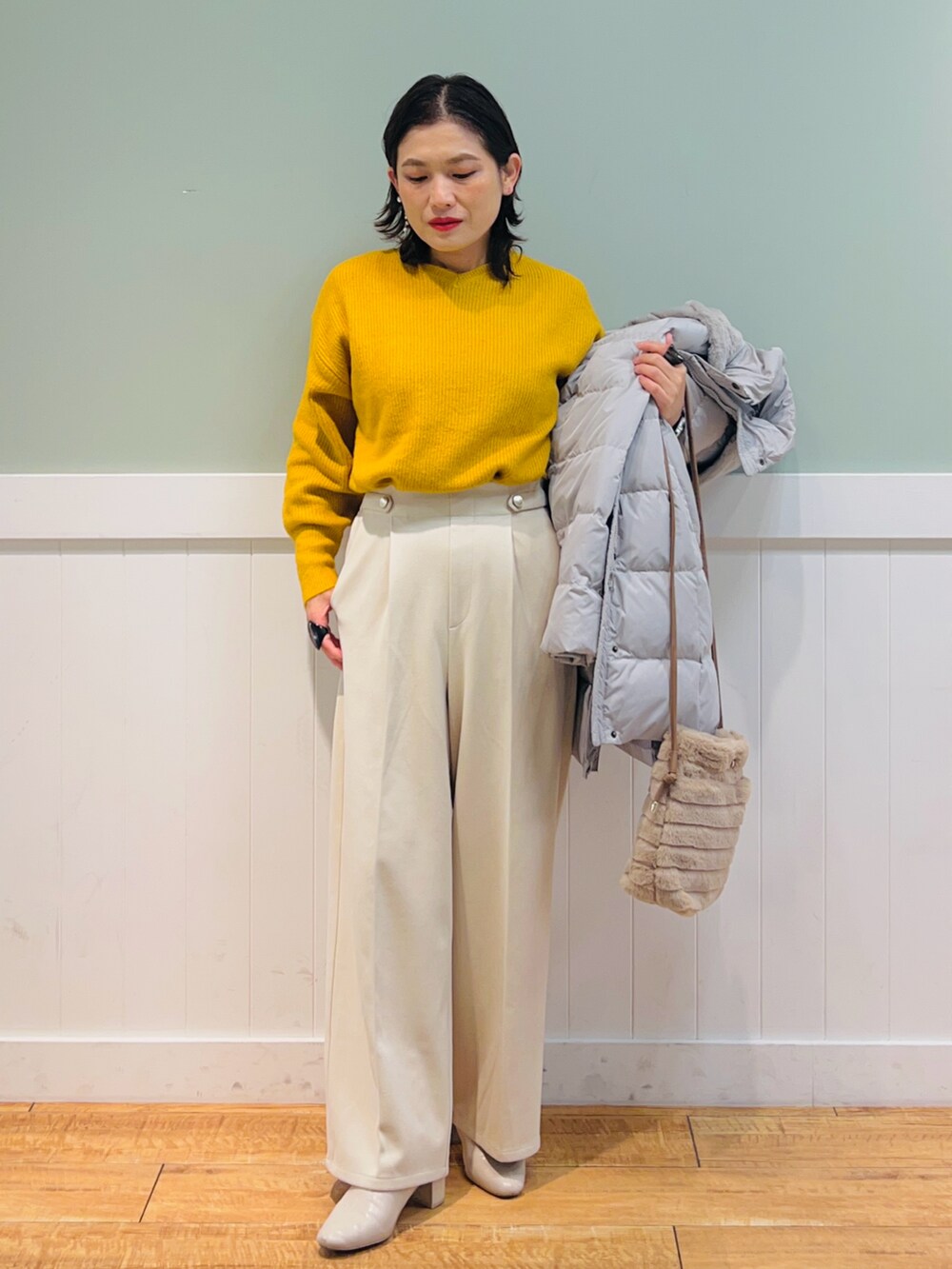 イエロー系のニット/セーター、ベージュ系のダウンジャケット/コート、ベージュ系のショルダーバッグを着用したレディースの冬コーディネートの3枚目の写真