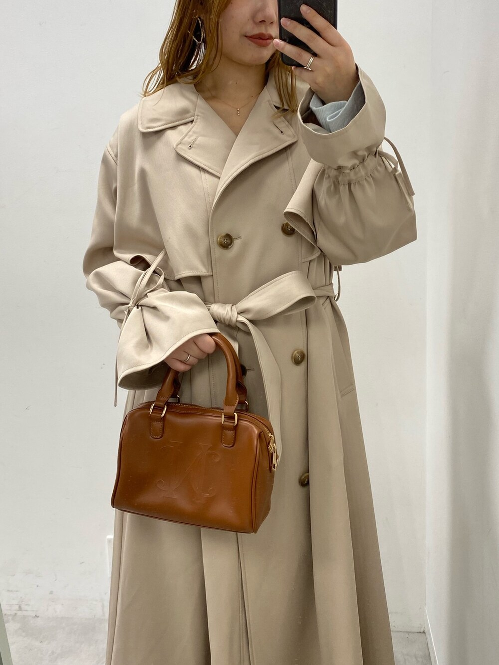 ベージュ系のトレンチコート、ブラウン系のボストンバッグ、ブルー系のデニムパンツを着用したレディースの冬コーディネートの2枚目の写真