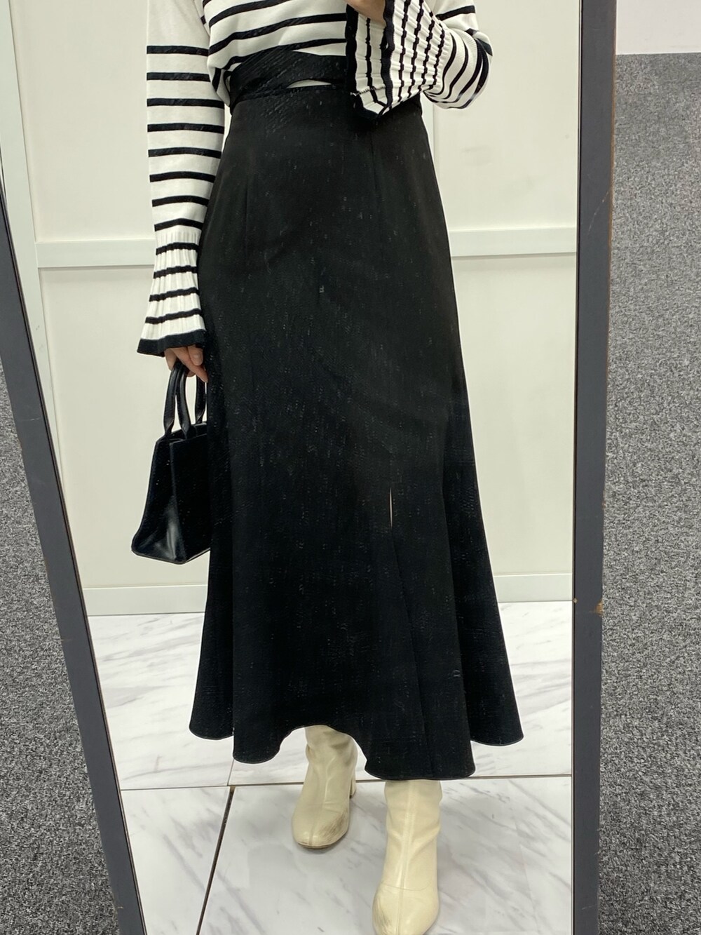 ブラック系のスカート、ブラック系のショルダーバッグ、ホワイト系のニット/セーターを着用したレディースの春コーディネートの2枚目の写真