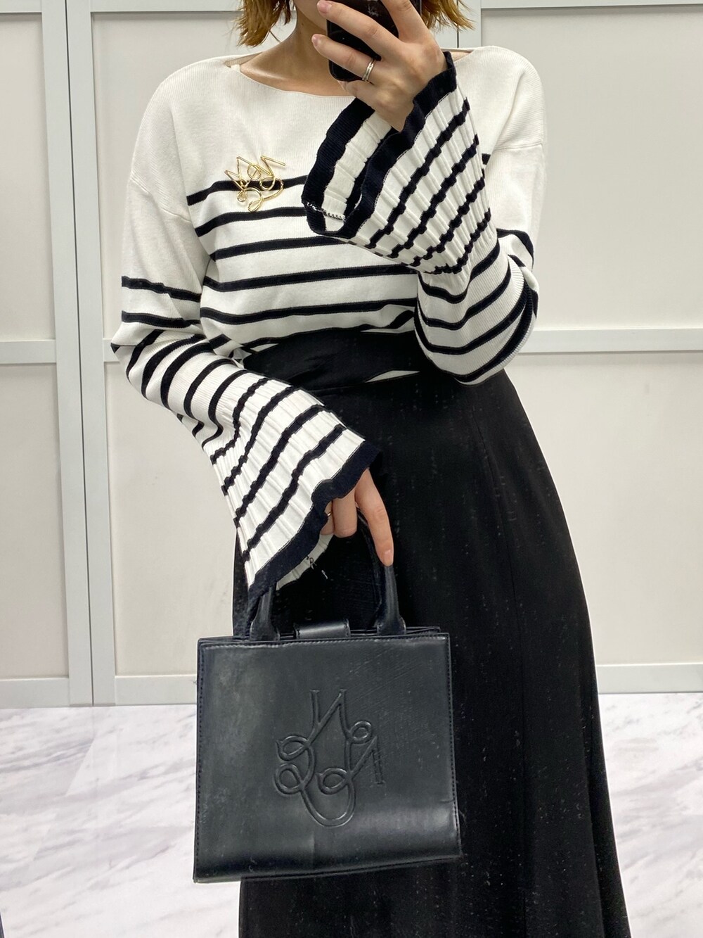 ブラック系のスカート、ブラック系のショルダーバッグ、ホワイト系のニット/セーターを着用したレディースの春コーディネートの3枚目の写真