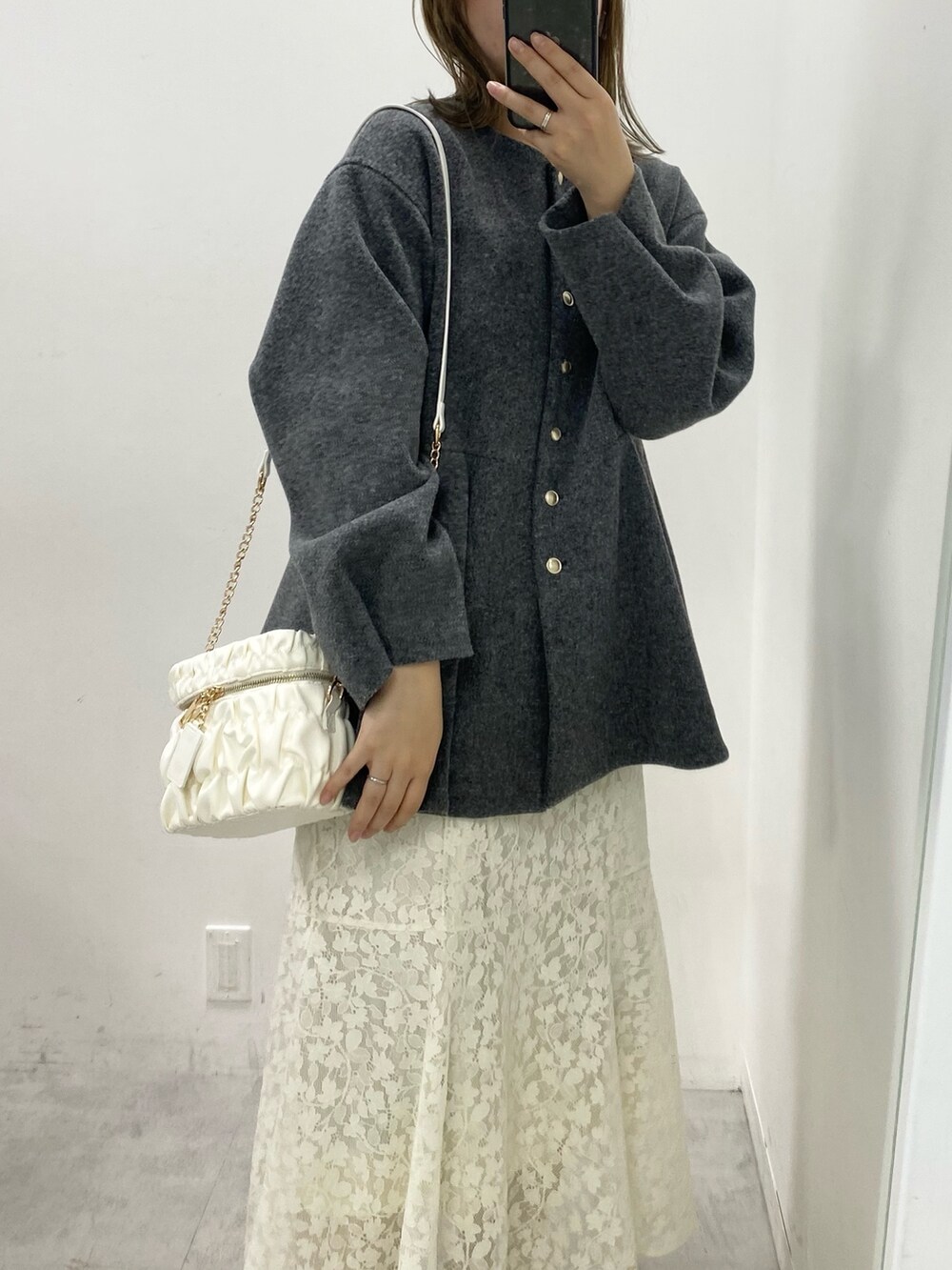 グレー系のノーカラーコート、ホワイト系のワンピース、ホワイト系のショルダーバッグを着用したレディースの冬コーディネートの2枚目の写真