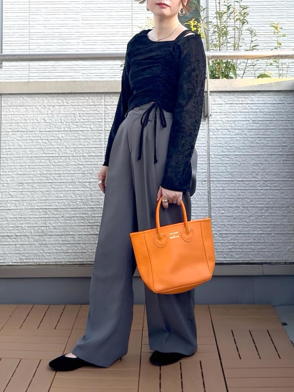 ブラック系のTシャツ/カットソー、グレー系のスラックス、オレンジ系のトートバッグを着用したレディースの秋コーディネートの2枚目の写真