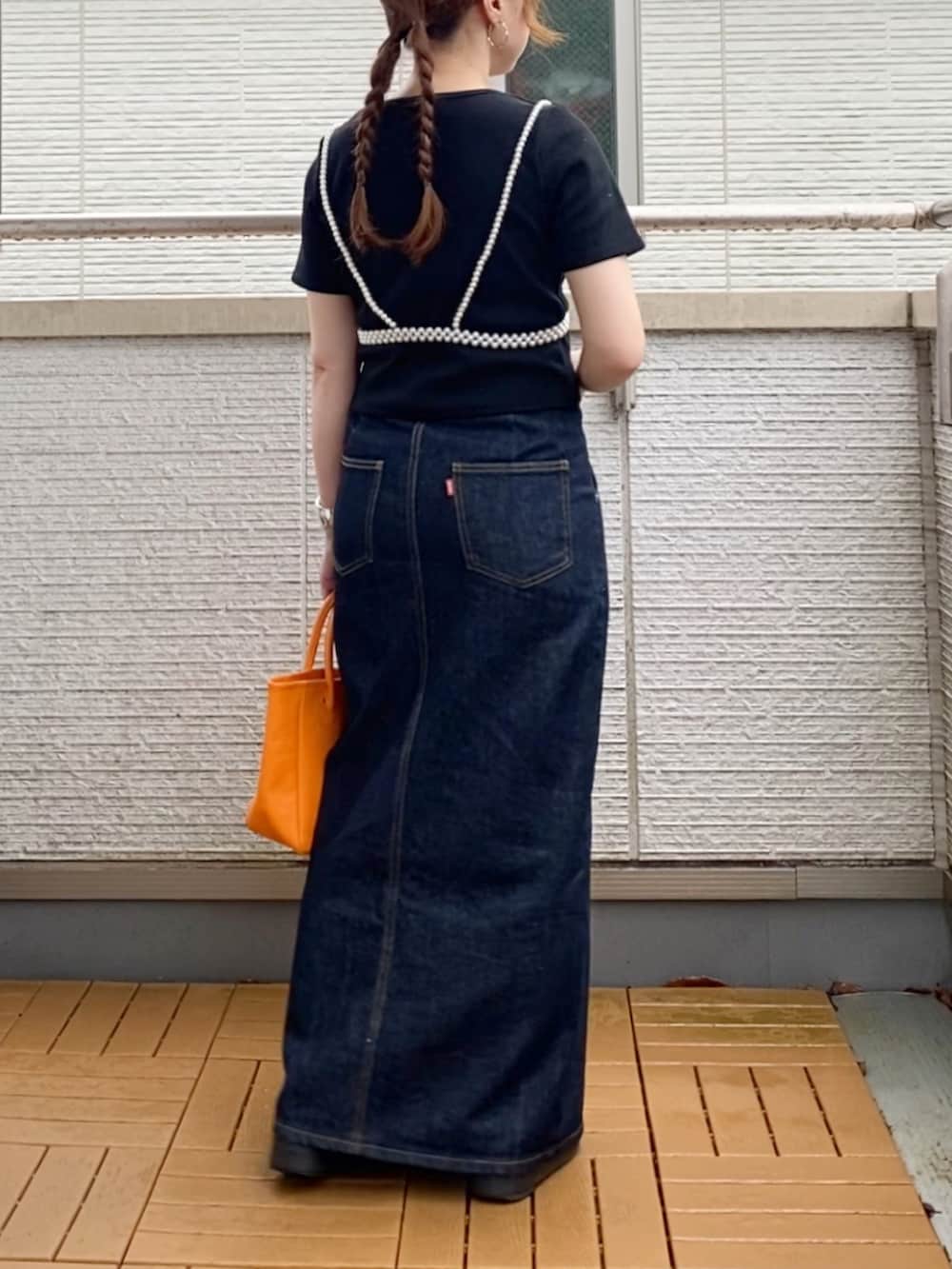ブラック系のTシャツ/カットソー、ブルー系のデニムスカート、オレンジ系のトートバッグを着用したレディースの夏コーディネートの3枚目の写真