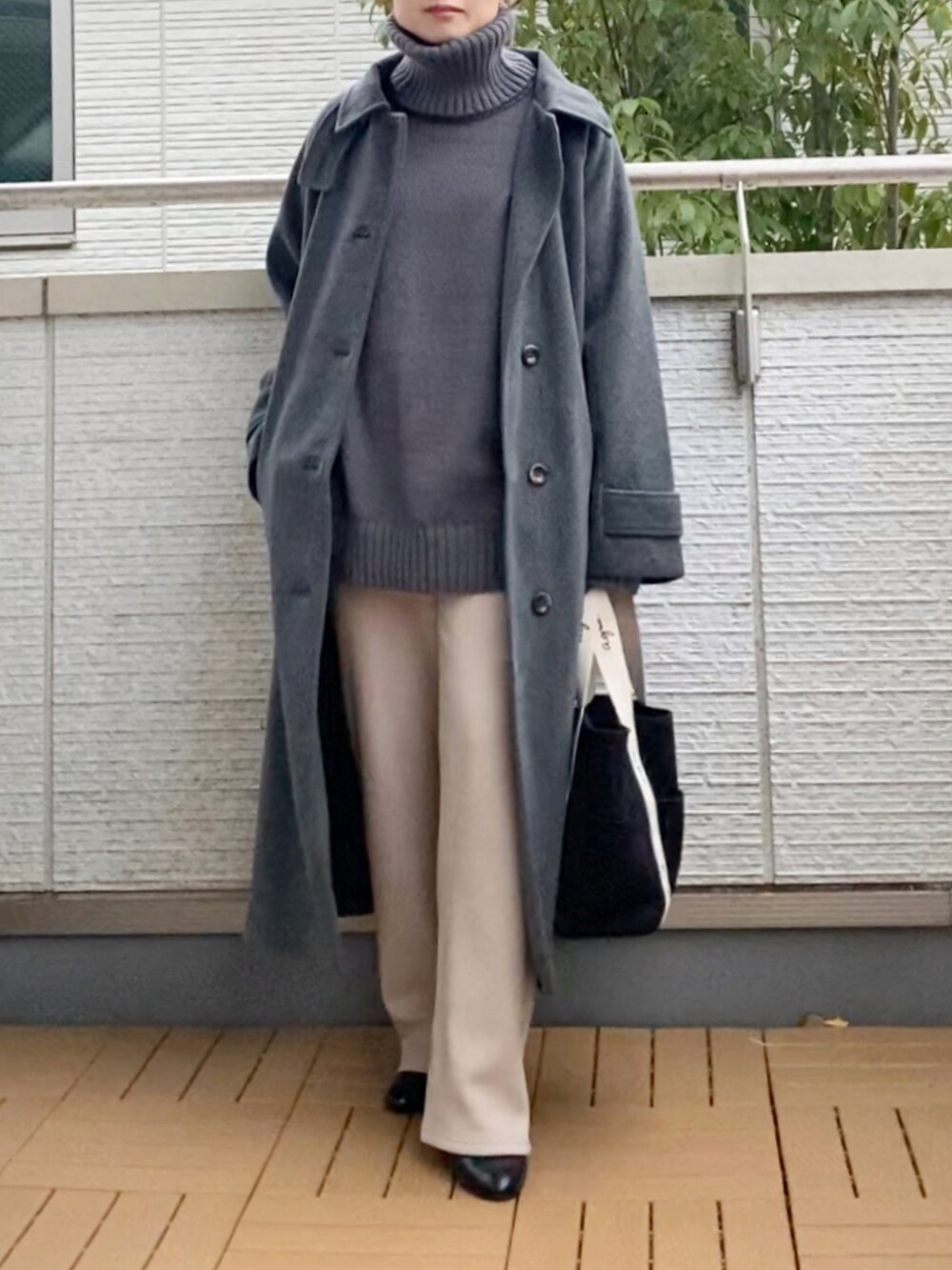 グレー系のステンカラーコート、グレー系のニット/セーター、ベージュ系のその他パンツを着用したレディースの冬コーディネートの2枚目の写真