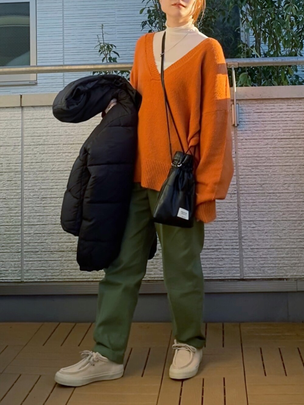 オレンジ系のニット/セーター、グリーン系のその他パンツ、ブラック系のダウンジャケット/コートを着用したレディースの冬コーディネートの2枚目の写真