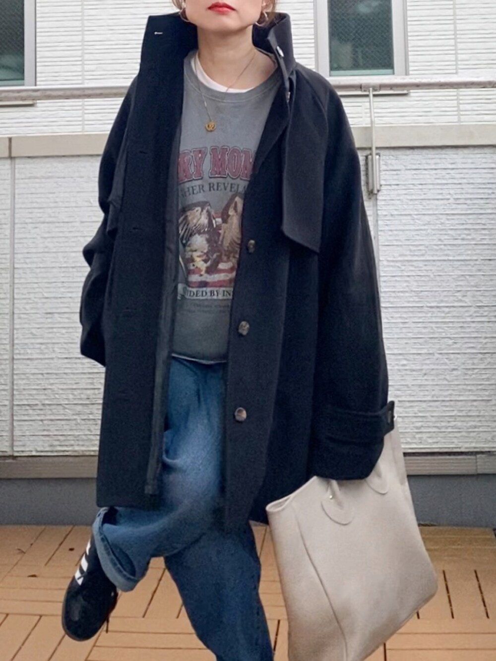 ブラック系のトレンチコート、グレー系のスウェット、ブルー系のデニムパンツを着用したレディースの秋コーディネートの5枚目の写真