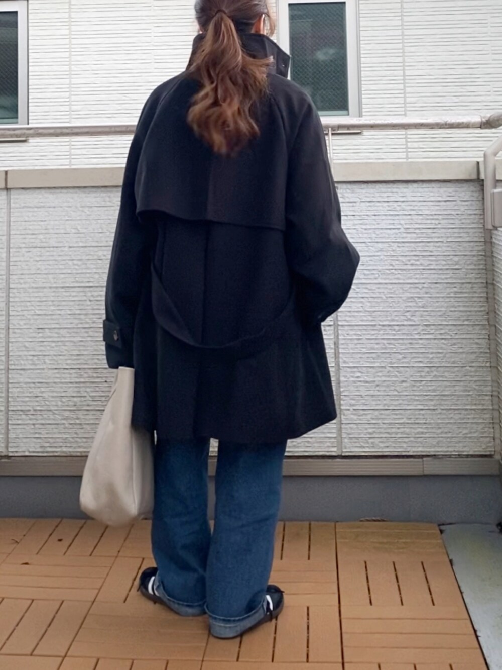 ブラック系のトレンチコート、グレー系のスウェット、ブルー系のデニムパンツを着用したレディースの秋コーディネートの4枚目の写真