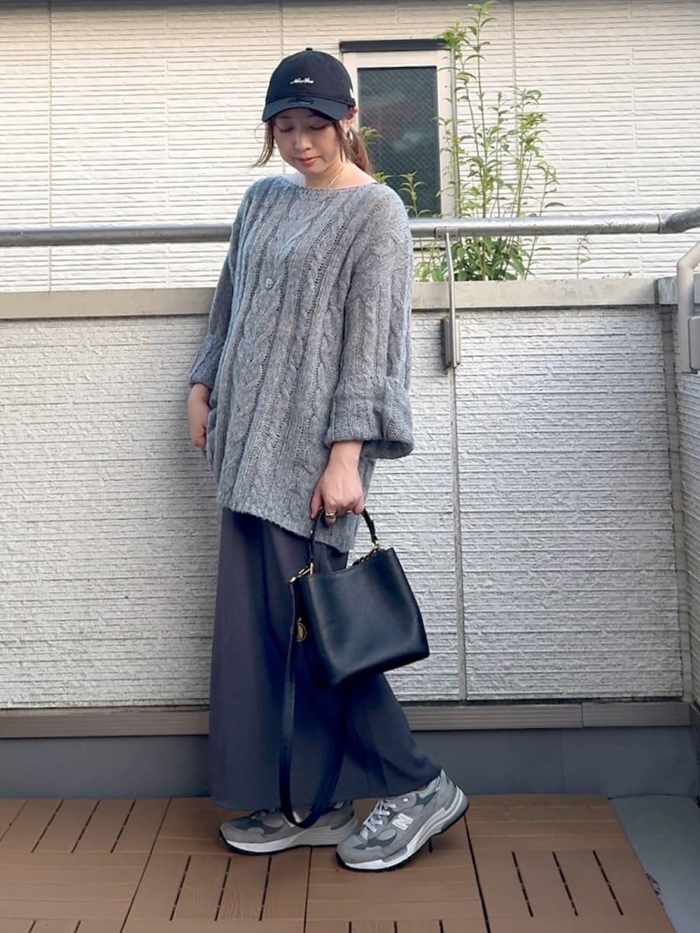 グレー系のニット/セーター、ブラック系のショルダーバッグ、グレー系のスカートを着用したレディースの夏コーディネートの2枚目の写真