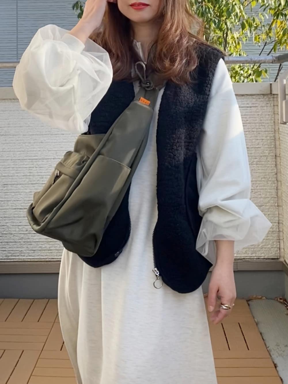 グレー系のワンピース、ブラック系のベスト、グリーン系のショルダーバッグを着用したレディースの春コーディネートの3枚目の写真