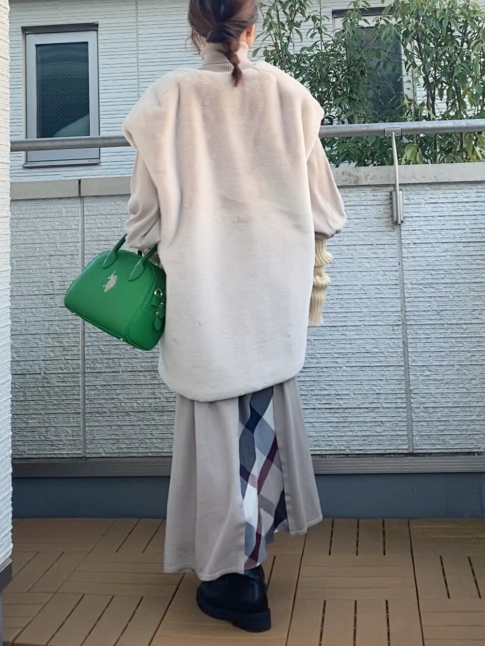 ベージュ系のワンピース、ホワイト系のベスト、グリーン系のハンドバッグを着用したレディースの冬コーディネートの3枚目の写真