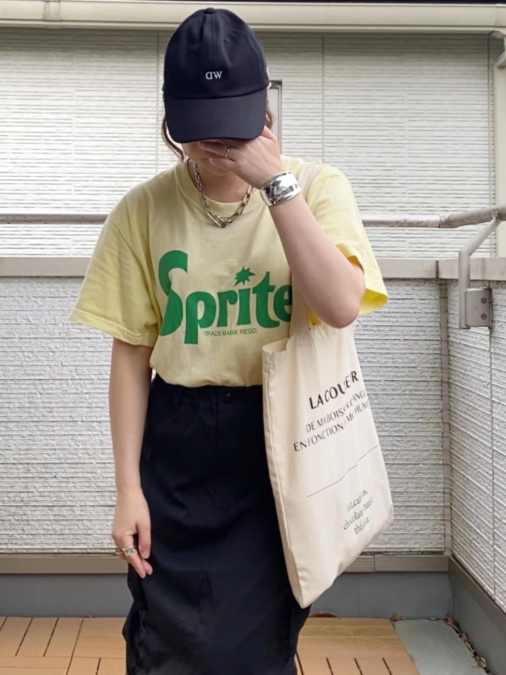 イエロー系のTシャツ/カットソー、ブラック系のスカート、ホワイト系のトートバッグを着用したレディースの夏コーディネートの3枚目の写真