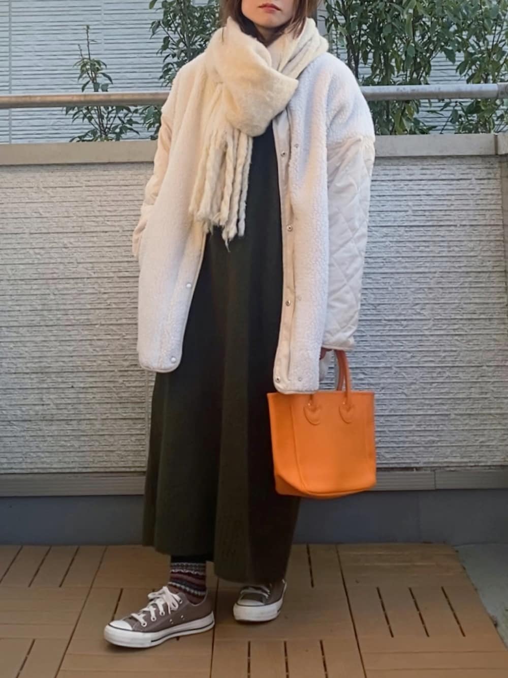 グリーン系のワンピース、ホワイト系のノーカラージャケット、オレンジ系のトートバッグを着用したレディースの冬コーディネートの2枚目の写真