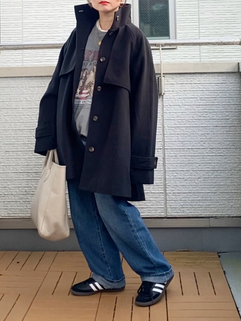 ブラック系のトレンチコート、グレー系のスウェット、ブルー系のデニムパンツを着用したレディースの秋コーディネートの2枚目の写真