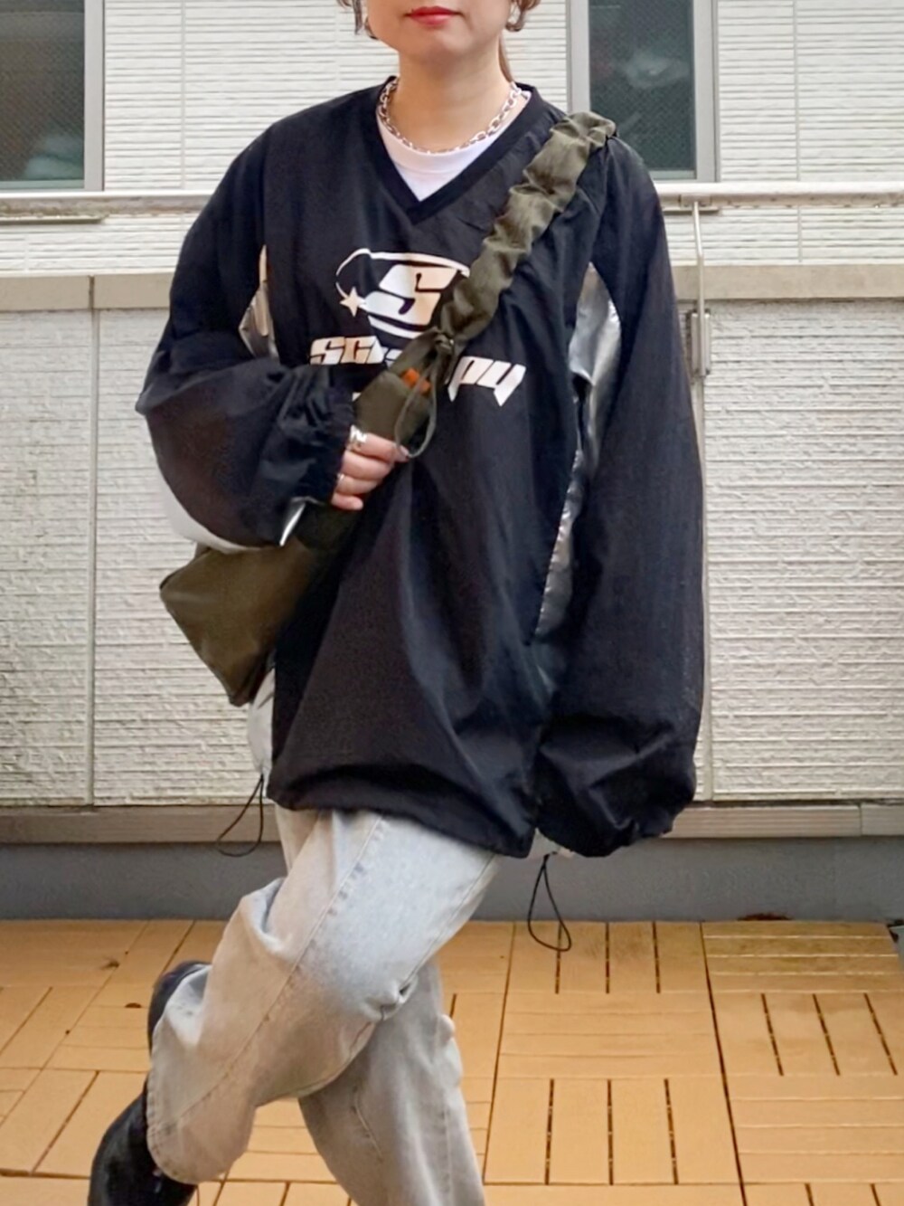 ブラック系のトップス、ブルー系のデニムパンツ、グリーン系のショルダーバッグを着用したレディースの秋コーディネートの5枚目の写真