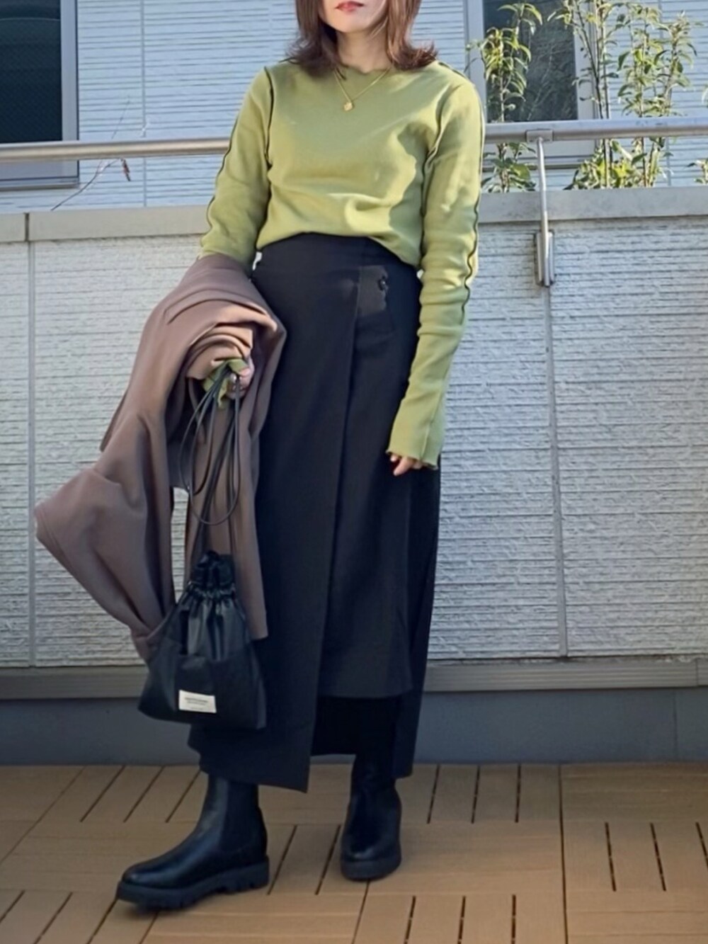 グリーン系のTシャツ/カットソー、ブラウン系のステンカラーコート、ブラック系のスカートを着用したレディースの冬コーディネートの2枚目の写真
