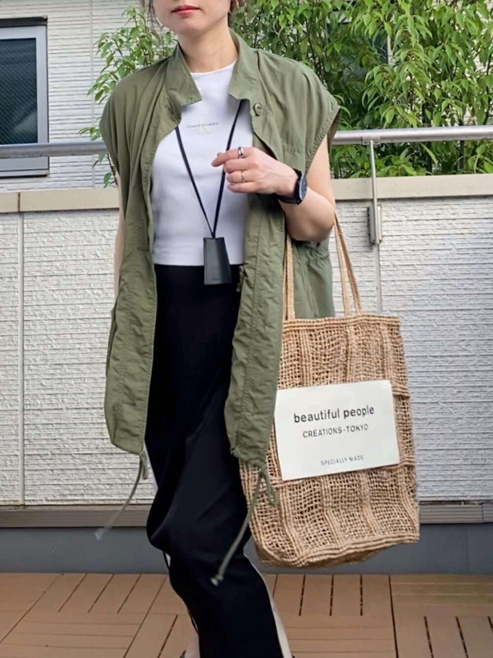 グリーン系のベスト、ホワイト系のTシャツ/カットソー、ブラック系のスカートを着用したレディースの夏コーディネートの2枚目の写真