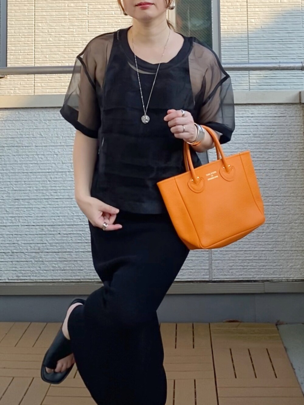 ブラック系のワンピース、ブラック系のTシャツ/カットソー、オレンジ系のトートバッグを着用したレディースの夏コーディネートの4枚目の写真