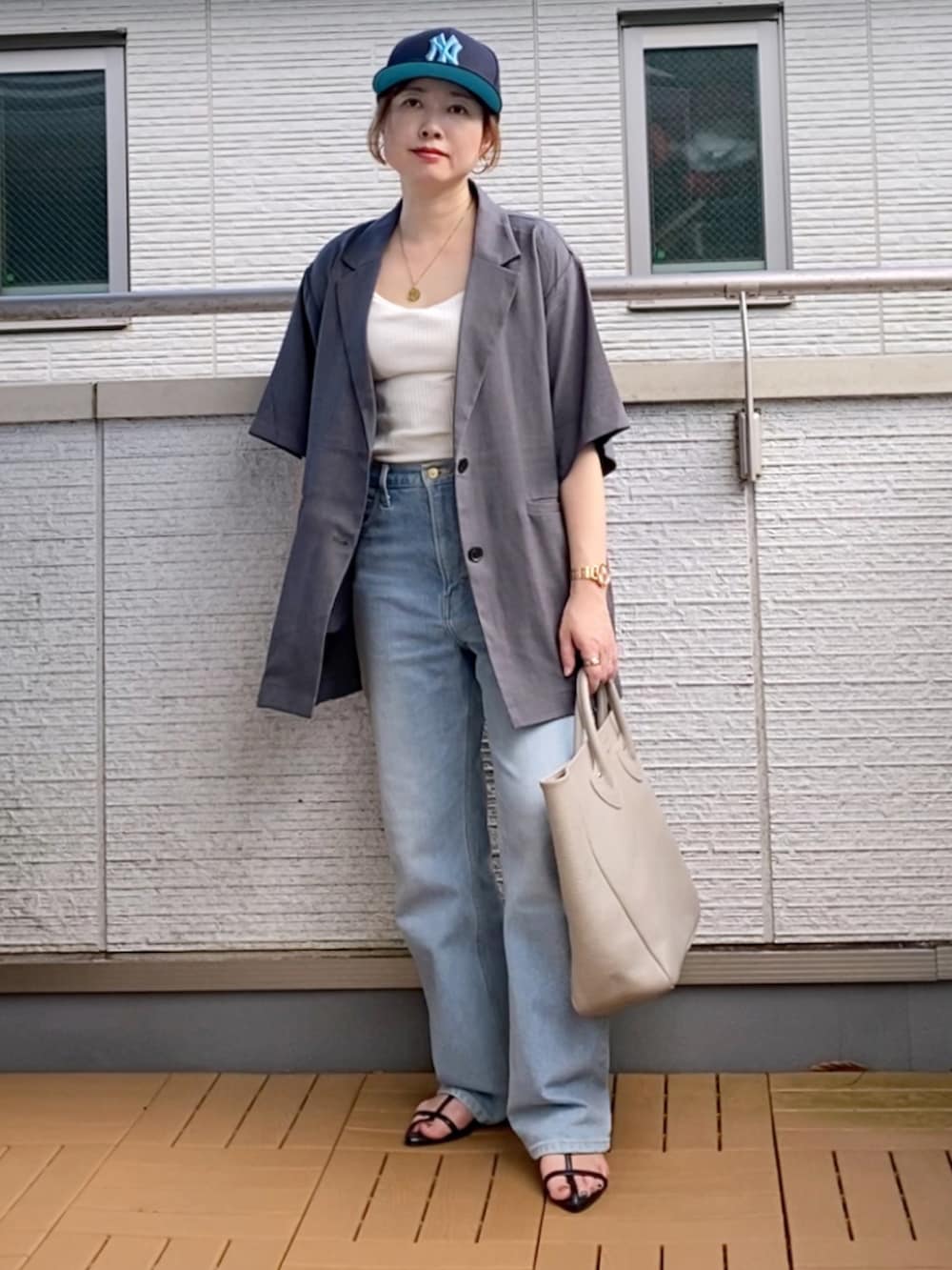 グレー系のテーラードジャケット、ホワイト系のタンクトップ、ブルー系のデニムパンツを着用したレディースの夏コーディネートの2枚目の写真