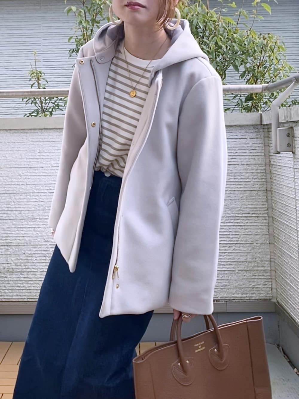 グレー系のノーカラーコート、ベージュ系のTシャツ/カットソー、ブルー系のデニムスカートを着用したレディースの秋コーディネートの2枚目の写真