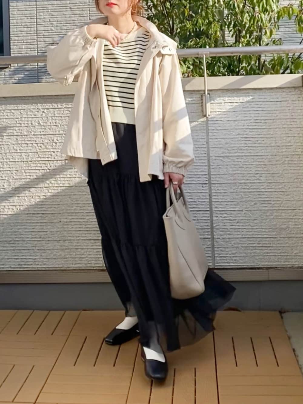 ホワイト系のマウンテンパーカー、ブラック系のカーディガン/ボレロ、ブラック系のスカートを着用したレディースの春コーディネートの3枚目の写真