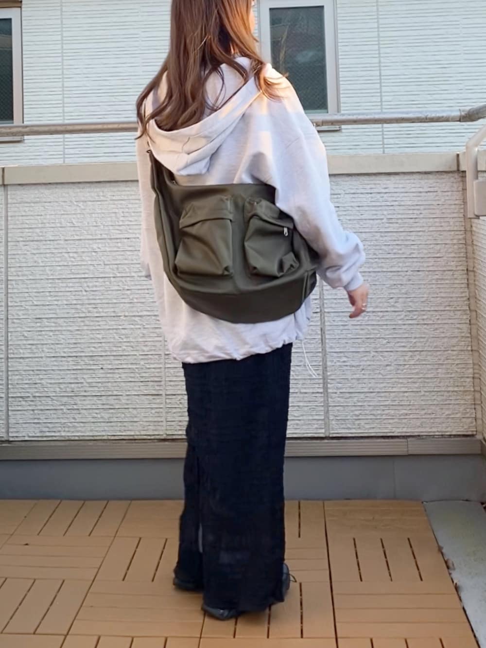 グレー系のパーカー、ブラック系のスカート、グリーン系のショルダーバッグを着用したレディースの冬コーディネートの3枚目の写真